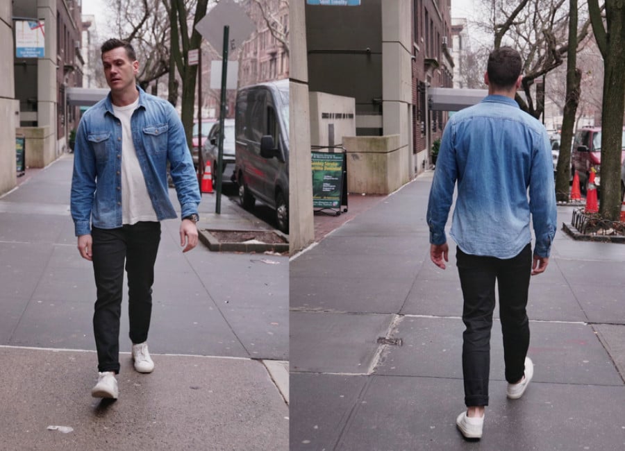 Nick wearing a light colored denim shirt, white t shirt, black jeans, and white leather sneakers
